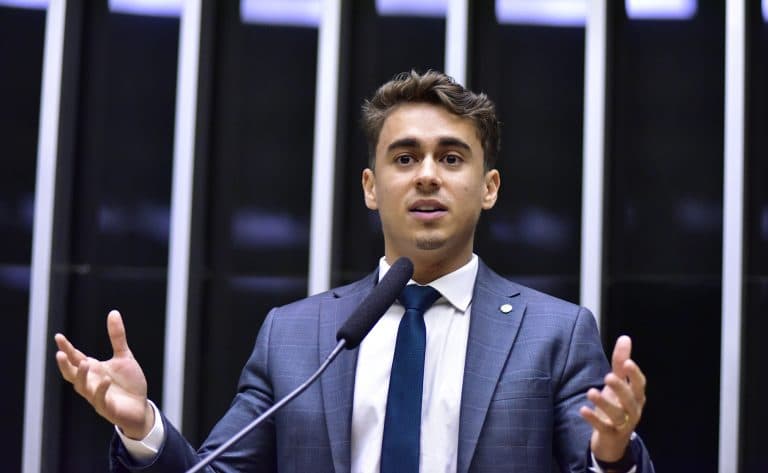 Fotografia de arquivo de Nikolas Ferreira discursando na tribuna da Câmara dos Deputados, com as mãos abertas. Não registra a decisão do TSE.