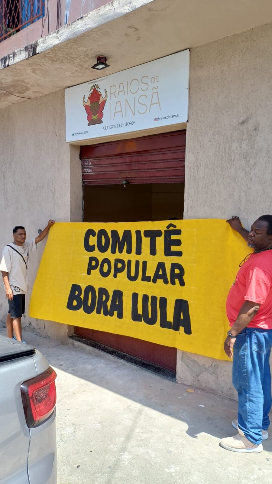 Duas pessoas seguram faixa amarela Comitê Popular Bora Lula diante de um estabelecimento em Belo Horizonte