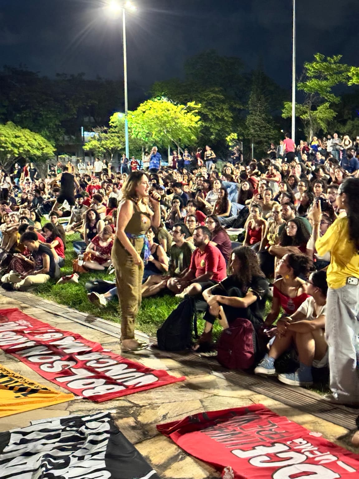 Bella Gonçalves fala ao microfone diante dos participantes da assembleia no gramado da UFMG