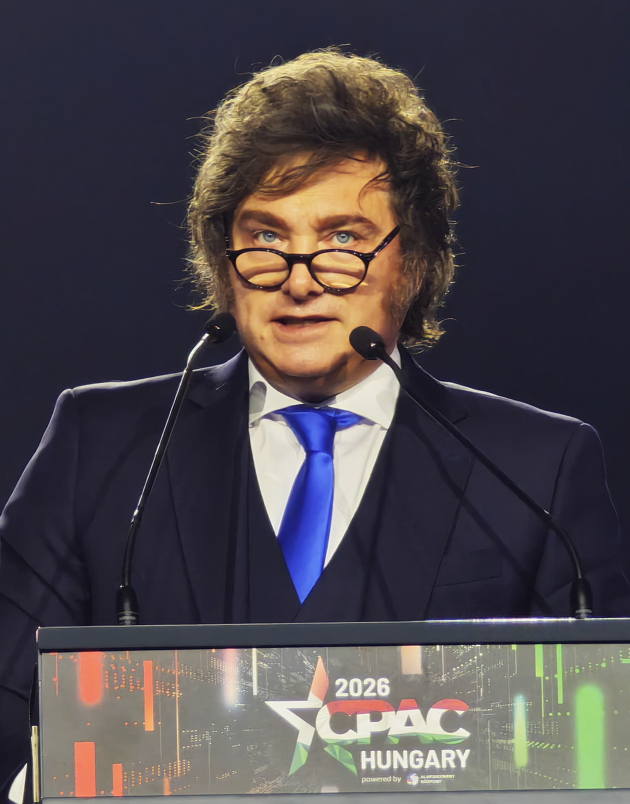 Fotografia de arquivo: Javier Milei, de terno e gravata azul, fala diante de dois microfones na CPAC em Budapeste, em 21 de março de 2026.