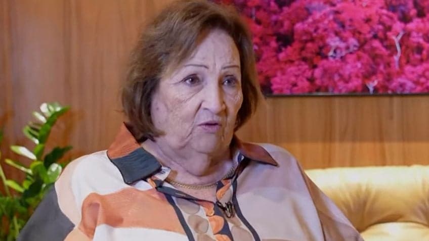Déa Lúcia, de camisa estampada, fala sentada em um sofá durante depoimento divulgado por Lula em 18 de outubro de 2026.