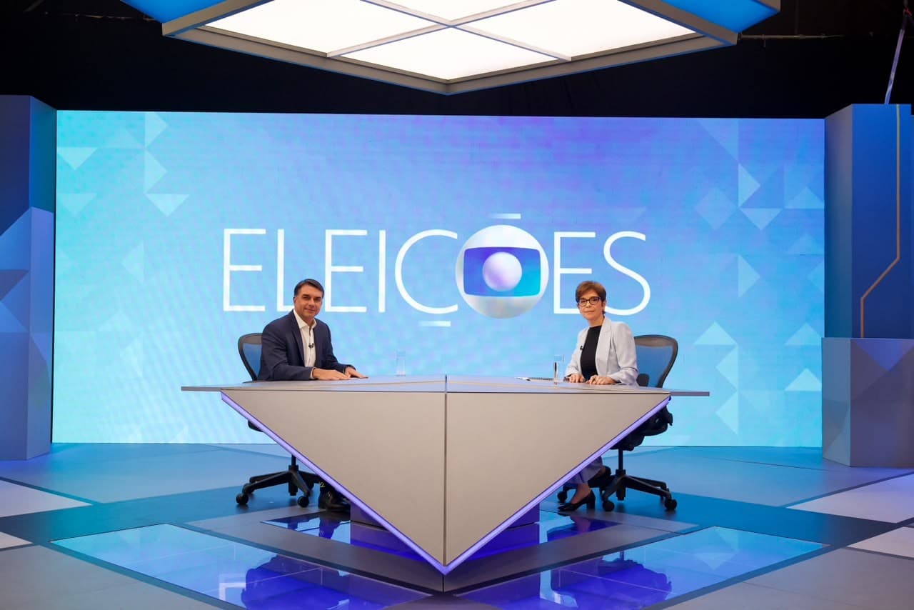 Flávio Bolsonaro e Renata Lo Prete sentados na bancada dos Estúdios Globo, antes da entrevista de 16 de outubro de 2026.