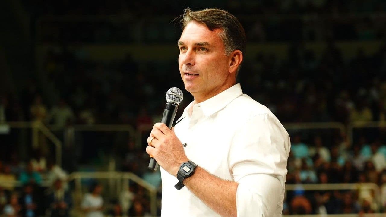 Flávio Bolsonaro de camisa branca, com microfone, em ato de campanha.
