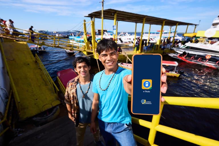 Integrantes da Comunidade Cipiá, em Manaus, apresentam um celular com o e-Título diante de embarcações. Foto de arquivo.