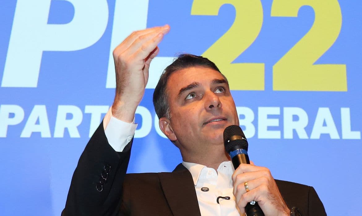 Flávio Bolsonaro discursa com um microfone diante de painel do Partido Liberal. Foto de arquivo.