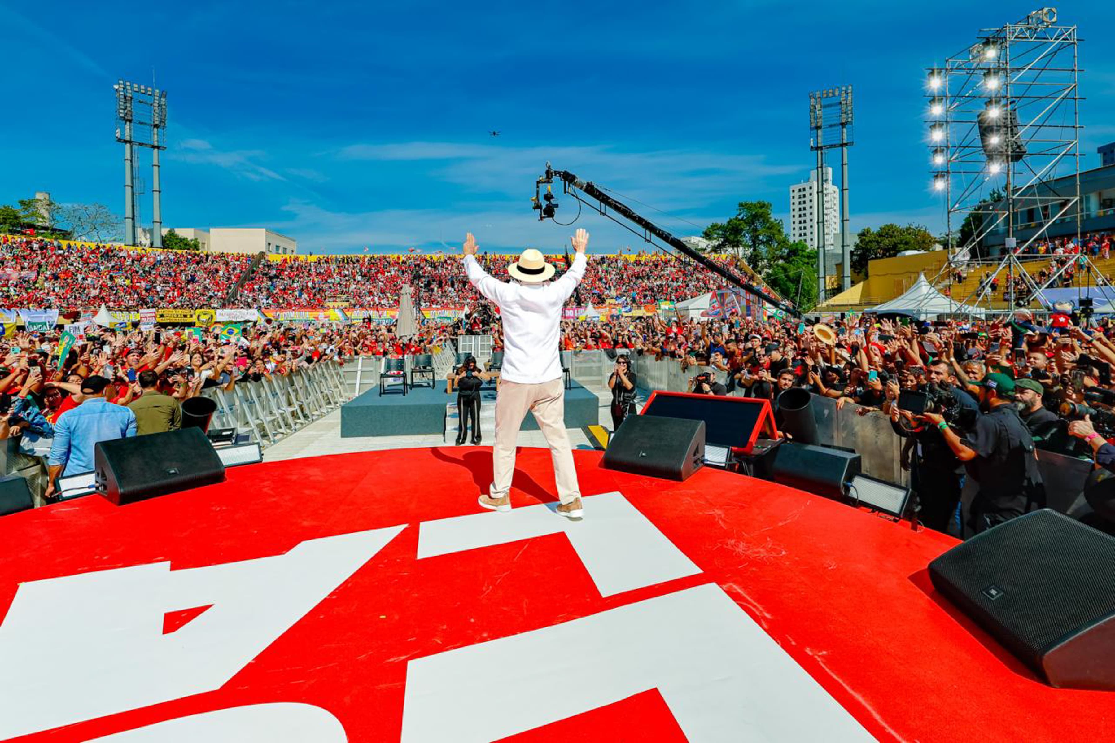 Lula de costas, com os braços erguidos diante do público no lançamento de sua campanha na Vila Euclides, São Bernardo do Campo, em 16 de agosto de 2026. Foto de arquivo, anterior ao anúncio da ação judicial.