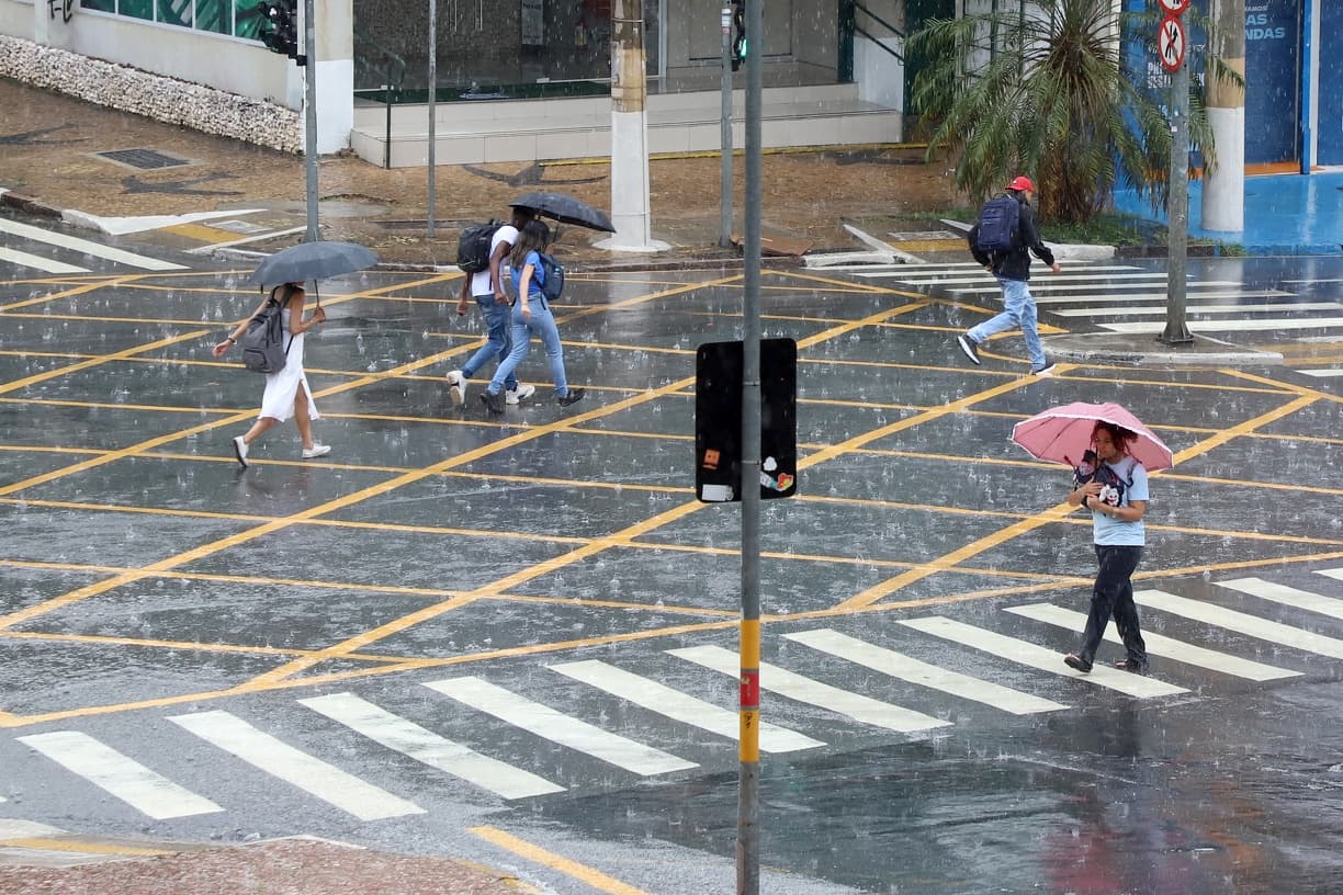 Fotografia de arquivo: pedestres com guarda-chuvas atravessam uma rua molhada em Campinas. A imagem ilustra a cobertura e não retrata o temporal de 11 de outubro.